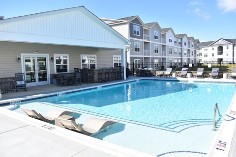 A swimming pool in front of a building with lounge chairs around it.