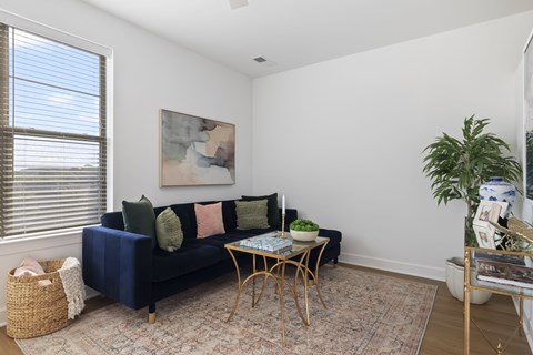 A living room with a blue couch and a painting on the wall.