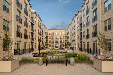 A courtyard with a bench and flower pots in front of apartment buildings.