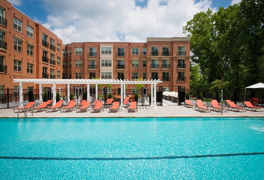 A large swimming pool in front of a red brick building with lounge chairs and umbrellas.