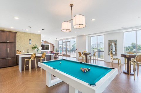 A pool table is in the middle of a room with a kitchen area in the background.