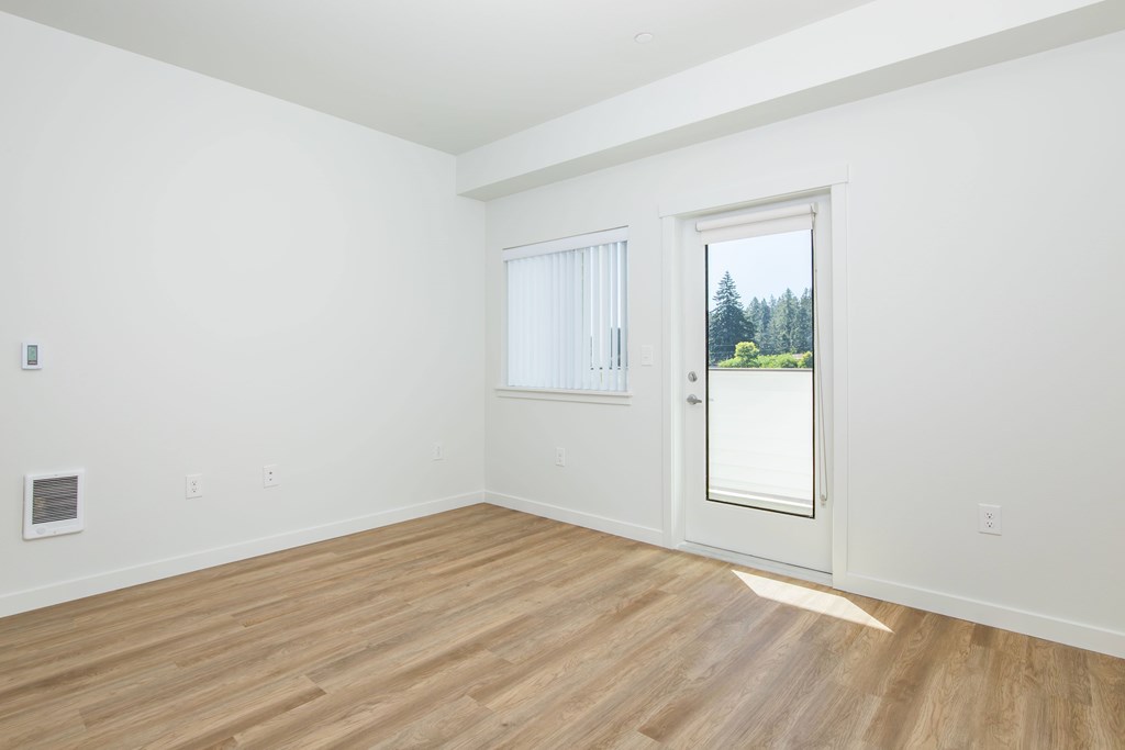 A room with a wooden floor and a door leading to a balcony with a view of trees.
