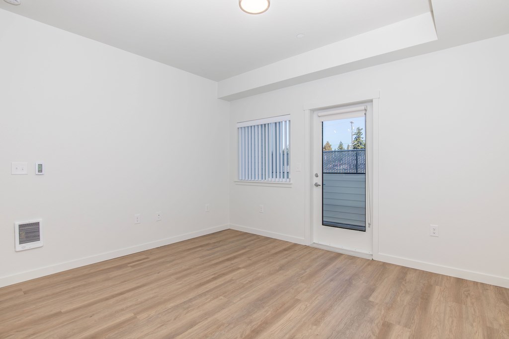 A room with a wooden floor and a window with a view of a fence and trees.