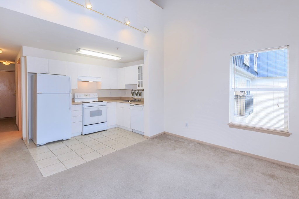 A kitchen with white appliances and a window with blinds.