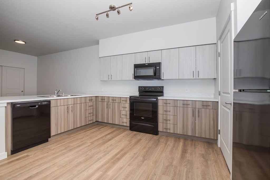 A modern kitchen with wooden floors and black appliances.
