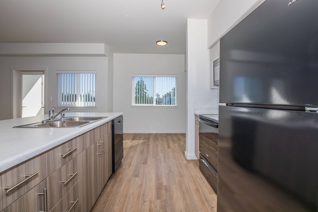 A modern kitchen with wooden floors and a black refrigerator.