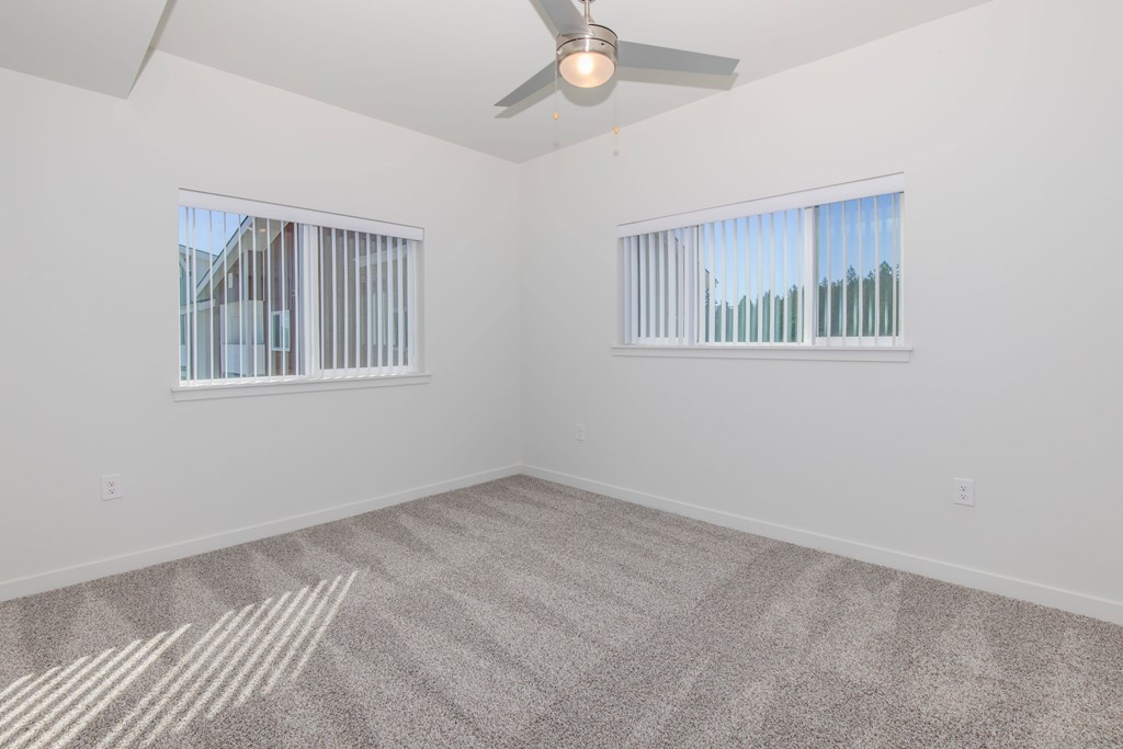 A room with a ceiling fan and two windows.