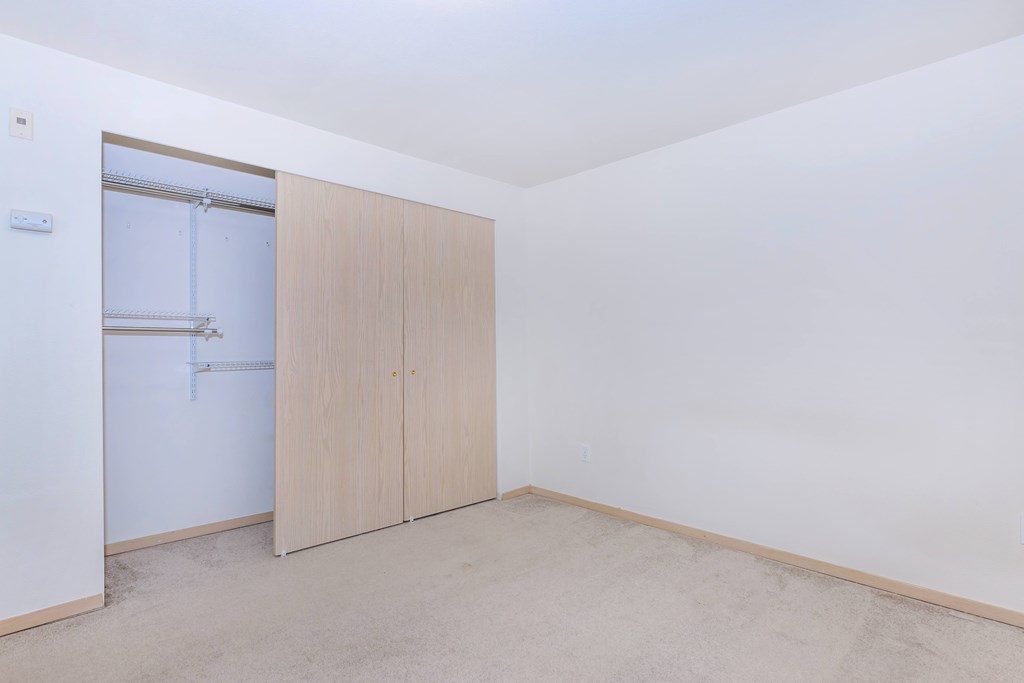 A room with a white wall and a brown floor with a wardrobe.