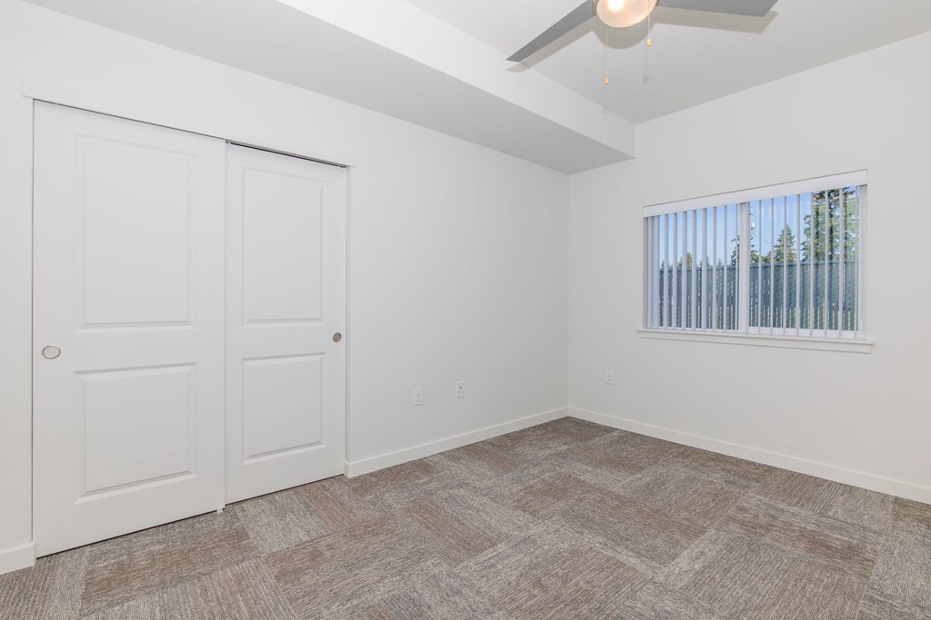 A room with a carpeted floor, a ceiling fan, and a window with blinds.