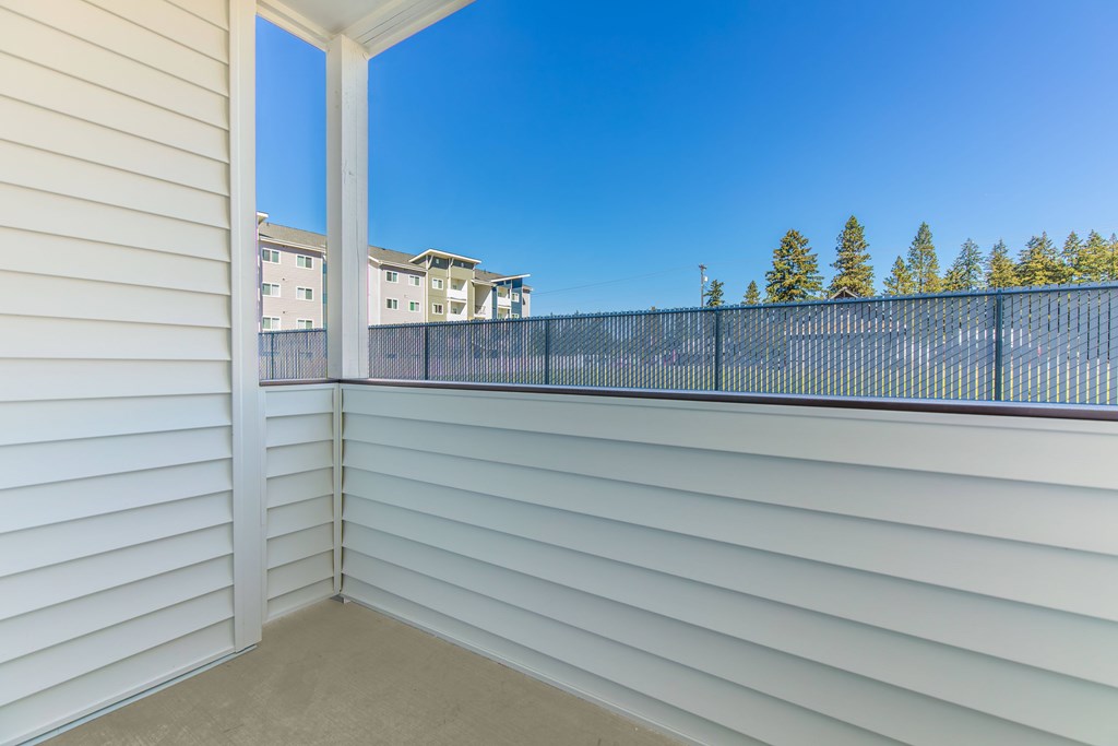A balcony with white walls and a black railing overlooks a residential area.