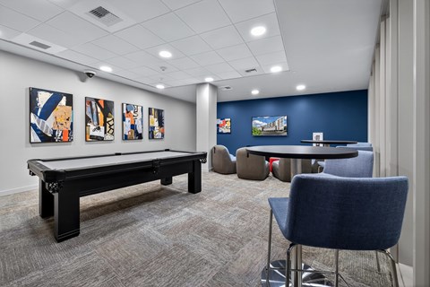 A room with a pool table, chairs, and paintings on the wall.