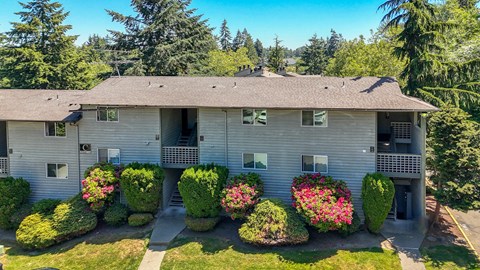 A house with a grey roof and a balcony surrounded by green bushes.