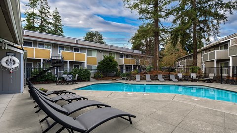A pool surrounded by lounge chairs in front of apartment buildings.