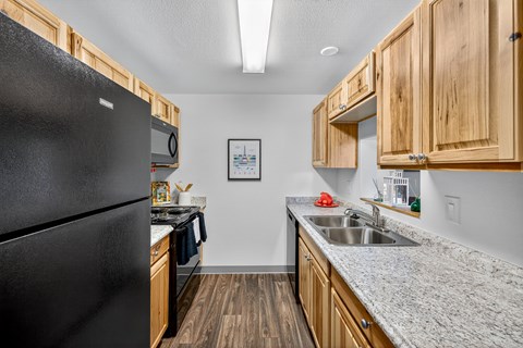 A kitchen with a black refrigerator and wooden cabinets.