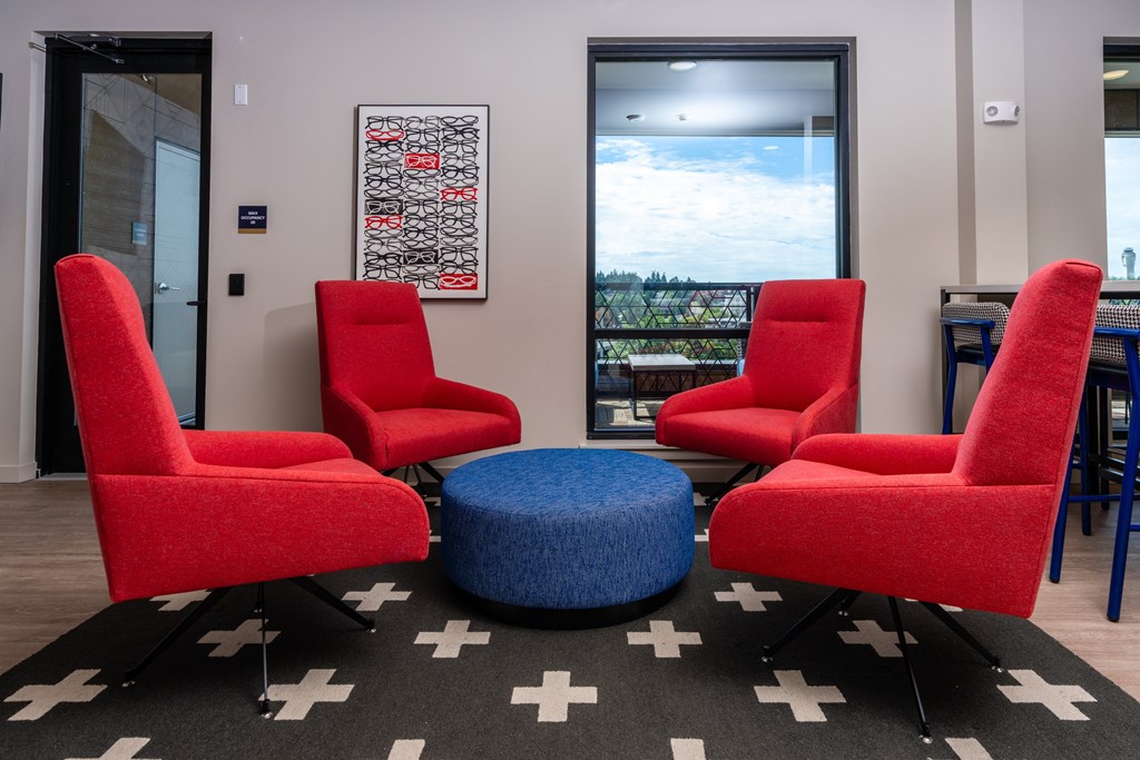 Four red chairs are arranged around a blue ottoman on a black and white rug.