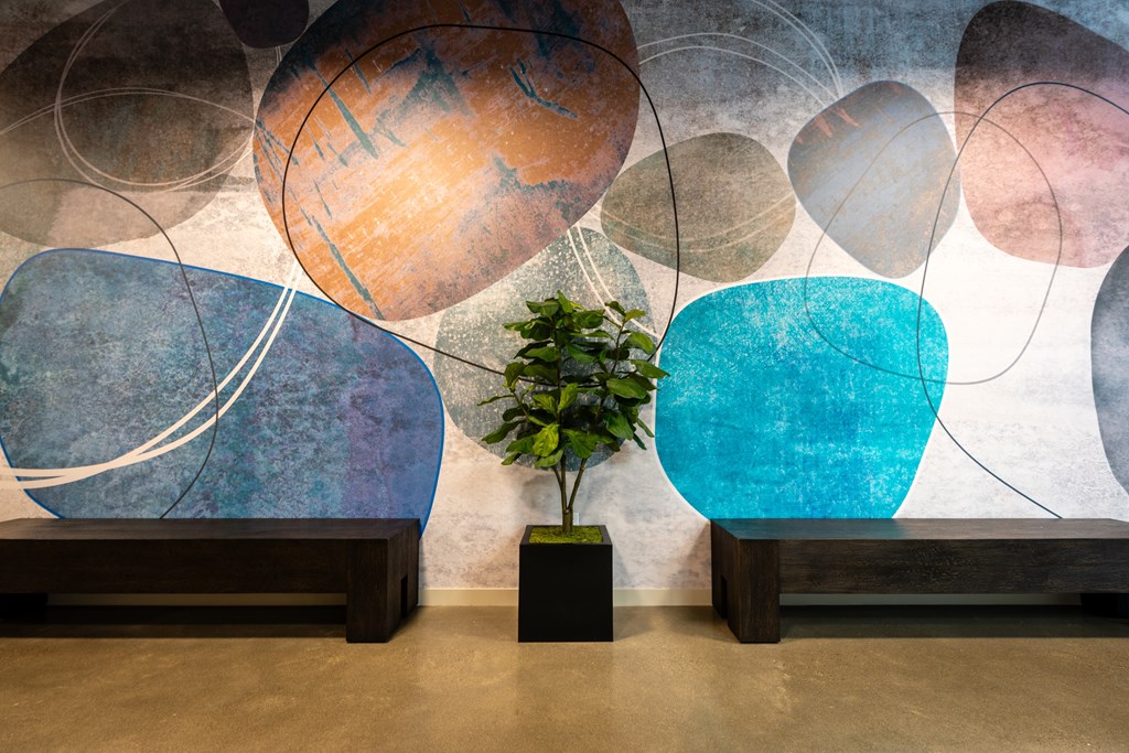 A plant sits in a pot in front of a wall with a large, colorful painting.