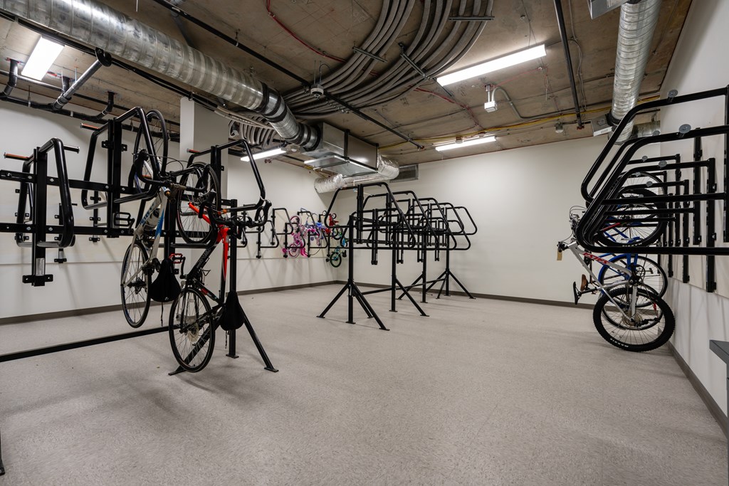 A room with a white wall and a grey floor has a lot of bicycles hanging on the wall.