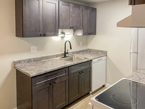 A kitchen with a granite countertop and dark brown cabinets.
