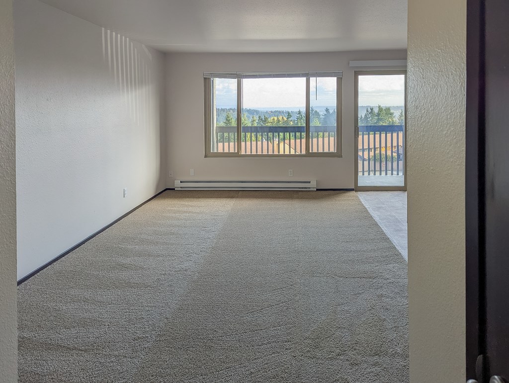 A room with a carpeted floor and a large window overlooking a balcony.