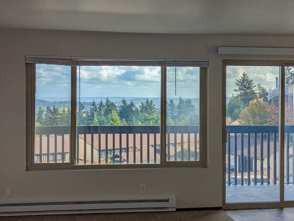 A room with a view of a forest and a building through the windows.