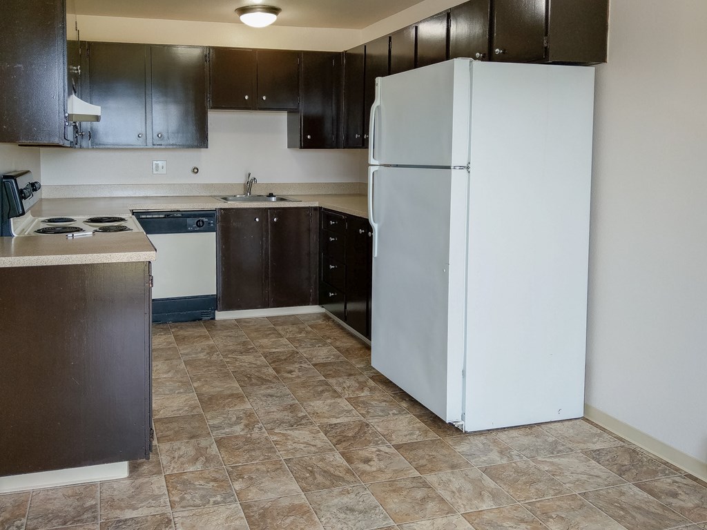 A kitchen with a white refrigerator and brown cabinets.