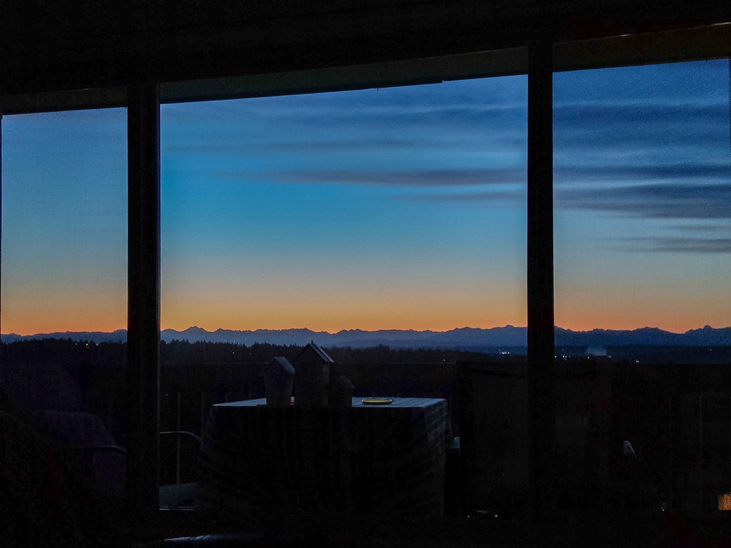 A view of a sunset through a window with a mountain range in the distance.