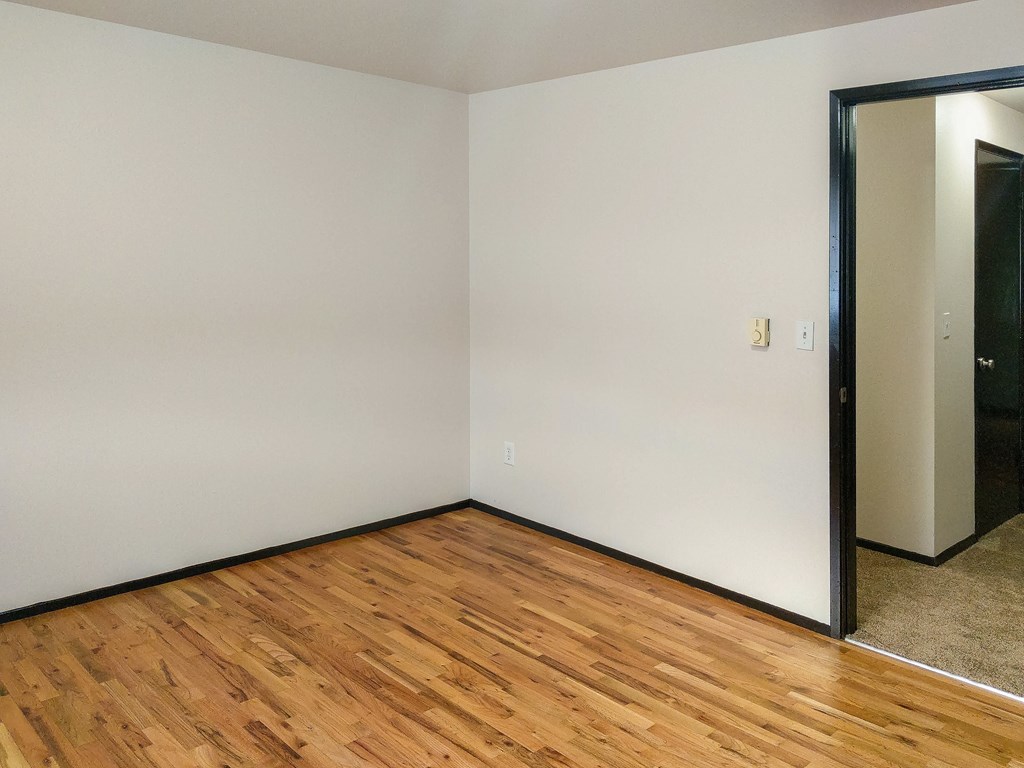 A room with wooden flooring and a white wall with a door.