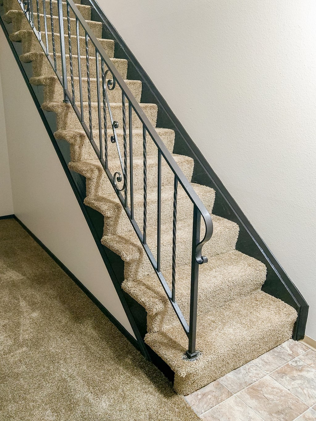 A staircase with a metal railing and beige carpeted steps.