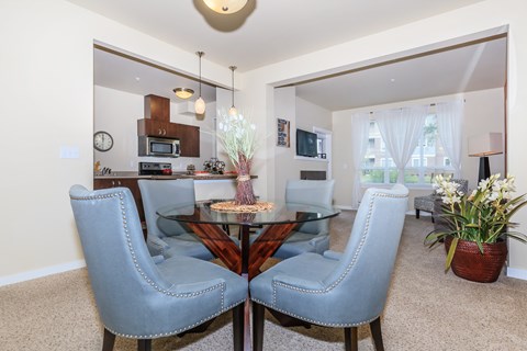 A dining room with a glass table and grey chairs.