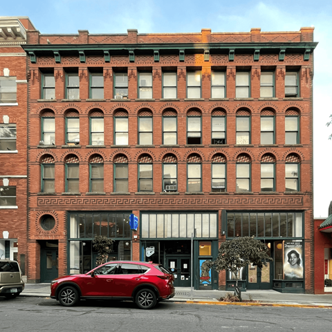 A red car is parked in front of a red brick building.