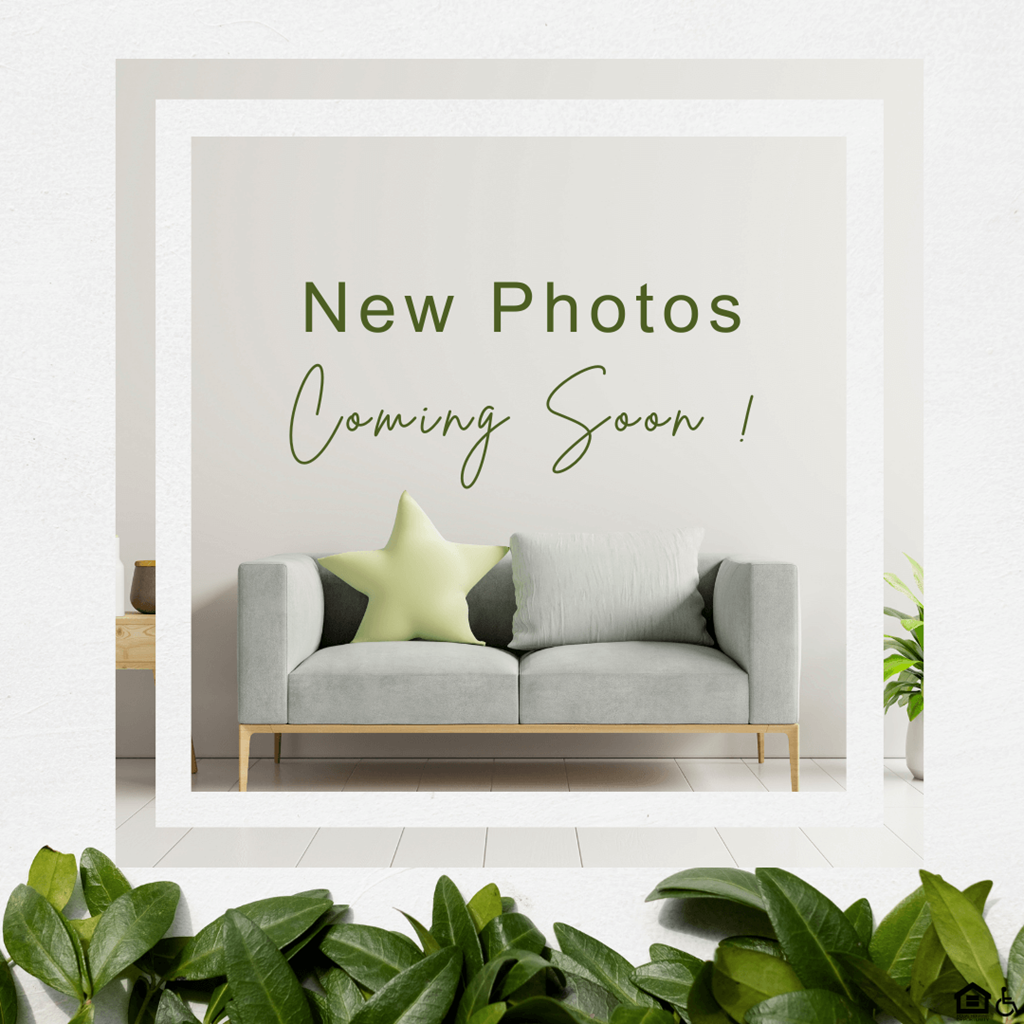 A poster with the text "New Photos Coming Soon !" is displayed on a wall above a grey sofa.