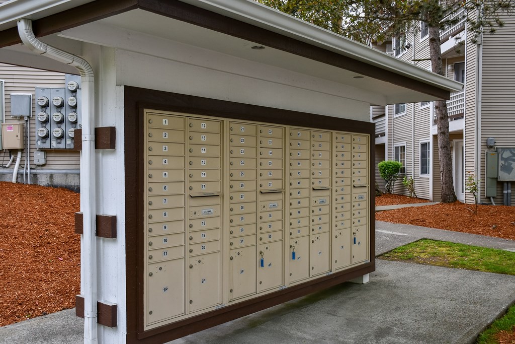 A brown mailbox with a white roof is in front of a building.
