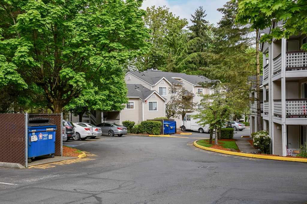 A parking lot with a blue recycling bin and a white car parked in front of a house.
