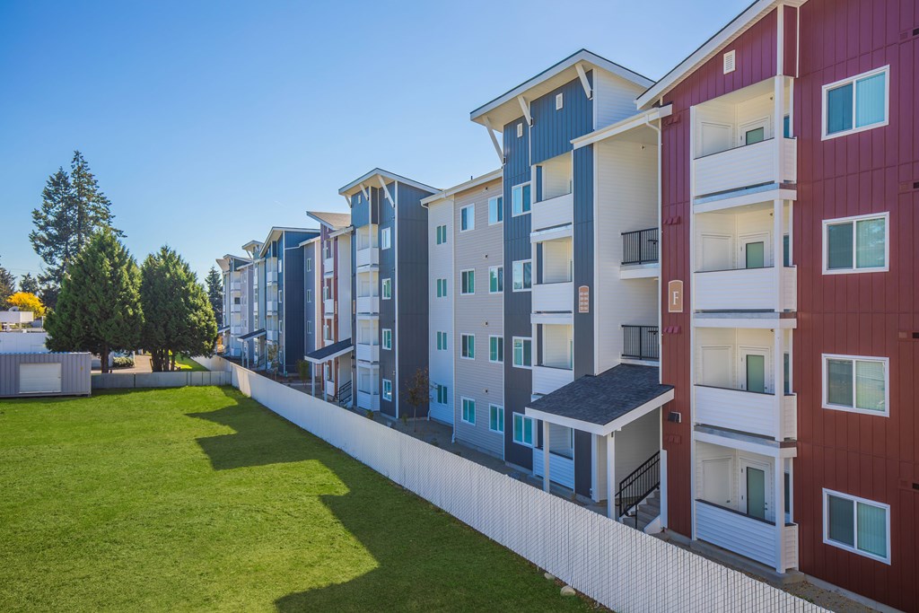 A row of modern apartment buildings with balconies and a green lawn in front.