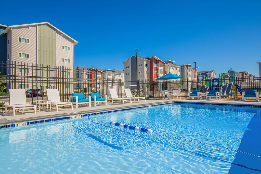 A swimming pool with lounge chairs and a playground in the background.