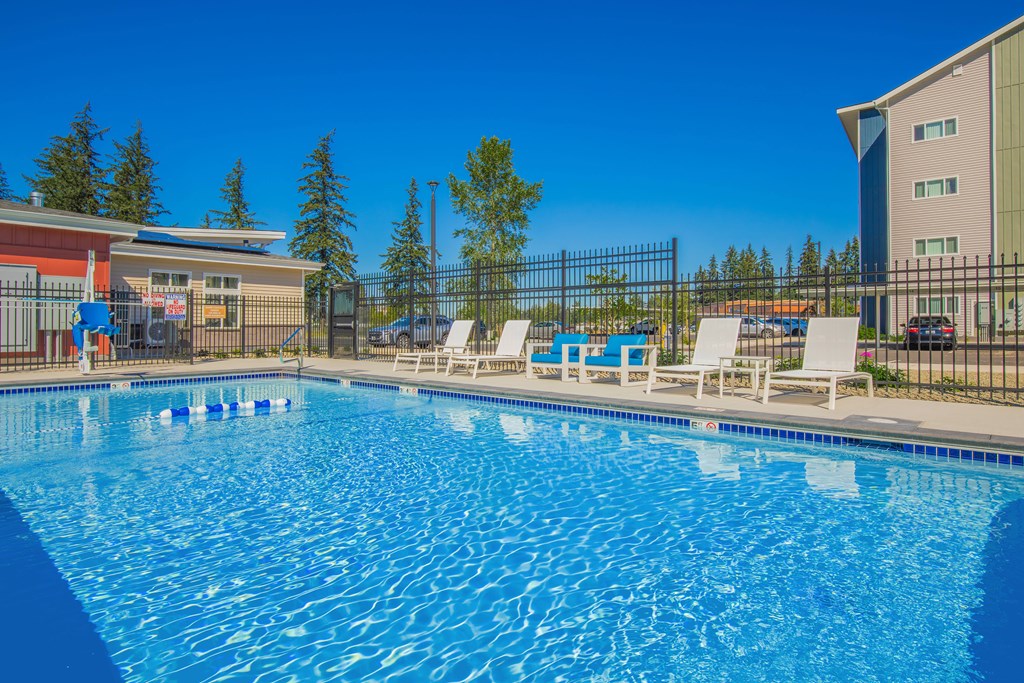 A large blue swimming pool with white lounge chairs and a fence around it.