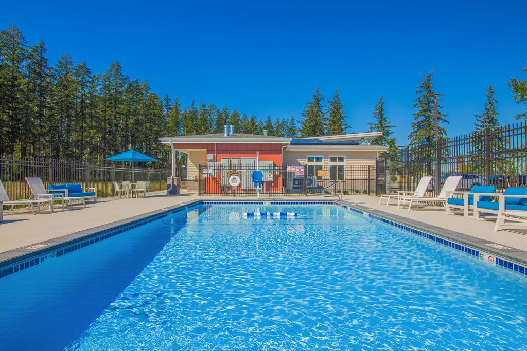 A large swimming pool with a blue umbrella and lounge chairs.
