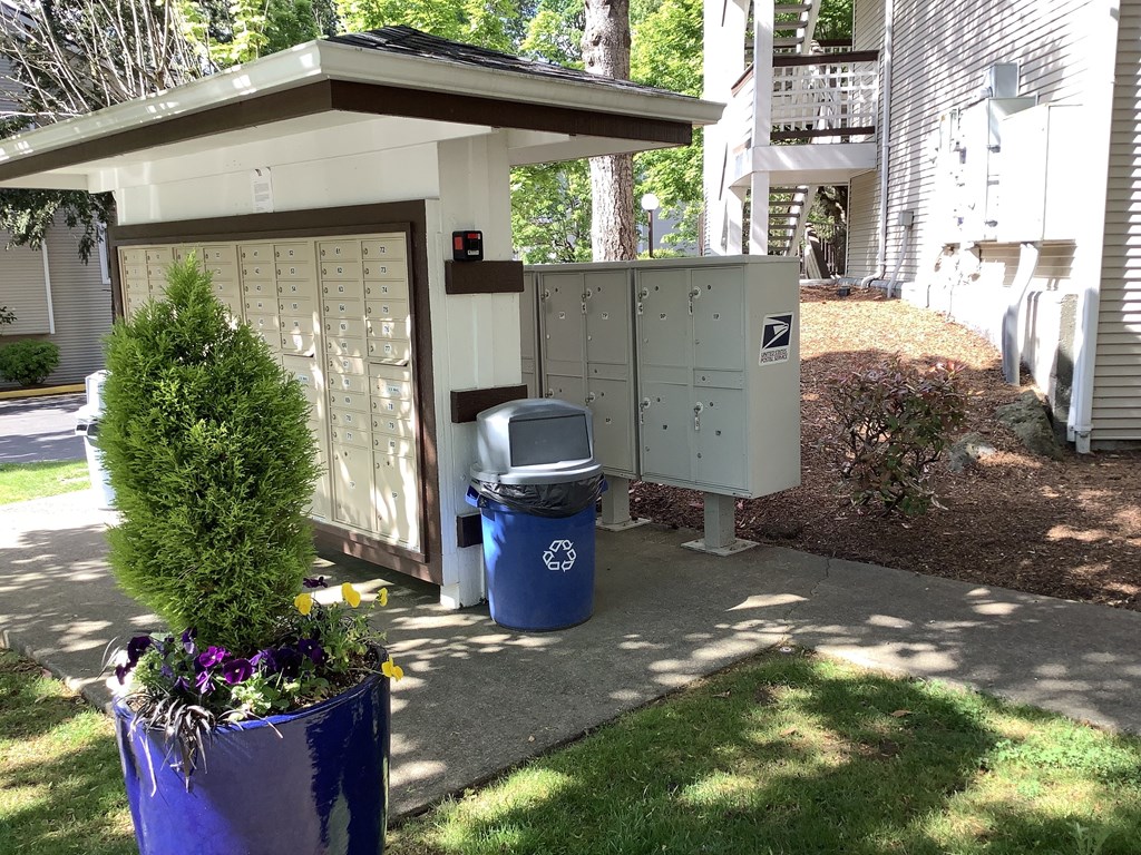 A mailbox is next to a trash can and a mailbox is on the other side of the fence.