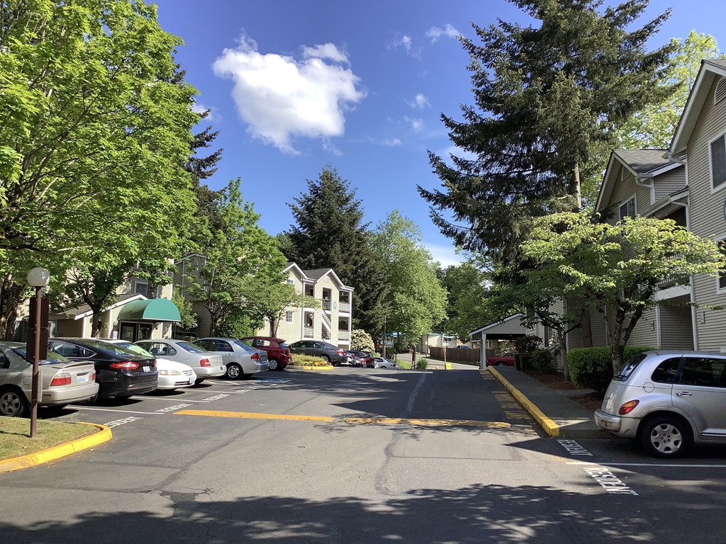 A street view with cars parked on the side and a white building in the background.