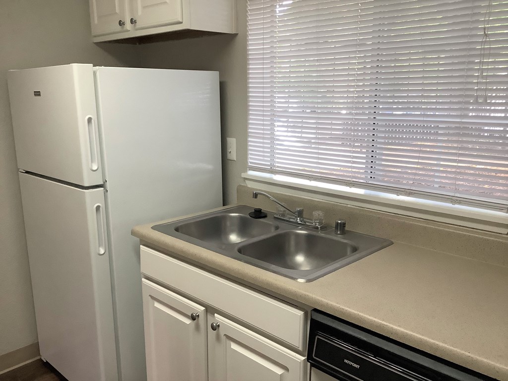 A white refrigerator stands next to a sink in a kitchen.
