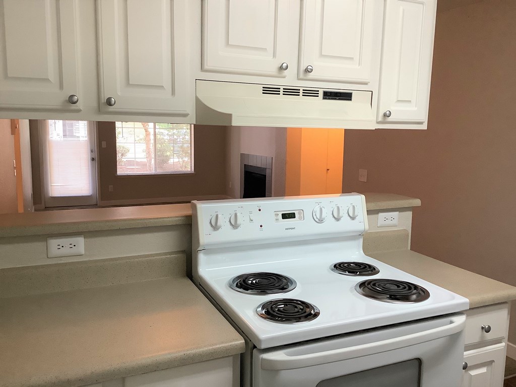 A white stove with four burners is in a kitchen with white cabinets.