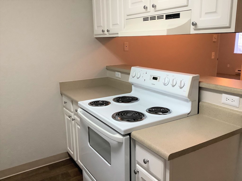 A white stove top oven with four burners and a white dishwasher in a kitchen.