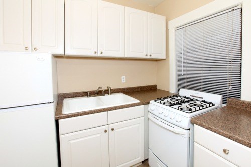 A white kitchen with a white fridge, white stove, and white cabinets.
