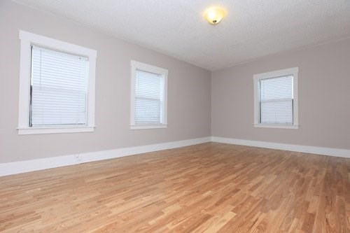 A room with wooden flooring and two windows.
