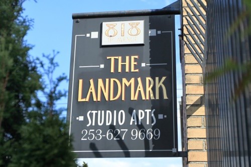 A sign for The Landmark Studio Apts with a phone number on it.