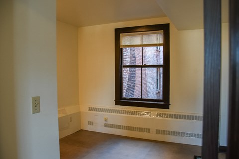 A window with blinds in a room with a white wall and a brown floor.