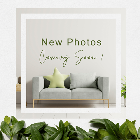 A poster with the text "New Photos Coming Soon !" is displayed on a wall above a grey sofa.