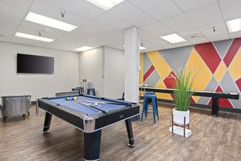 A pool table in a room with a TV mounted on the wall.