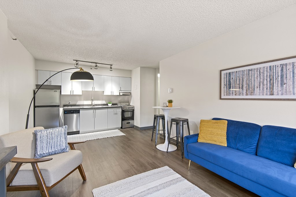 A blue couch sits in a living room with a white table and a bar area in the background.