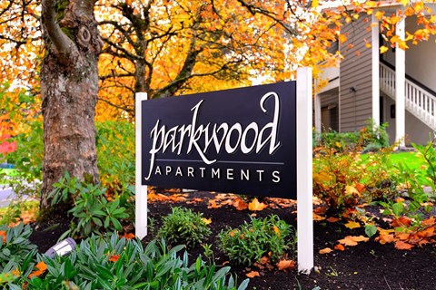 A sign for Parkwood Apartments is in front of a tree.